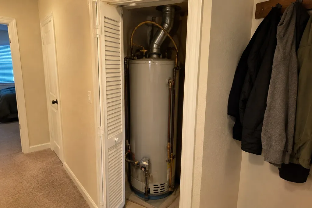 Old gas water heater squeezed into a cramped hall closet with a louvered door