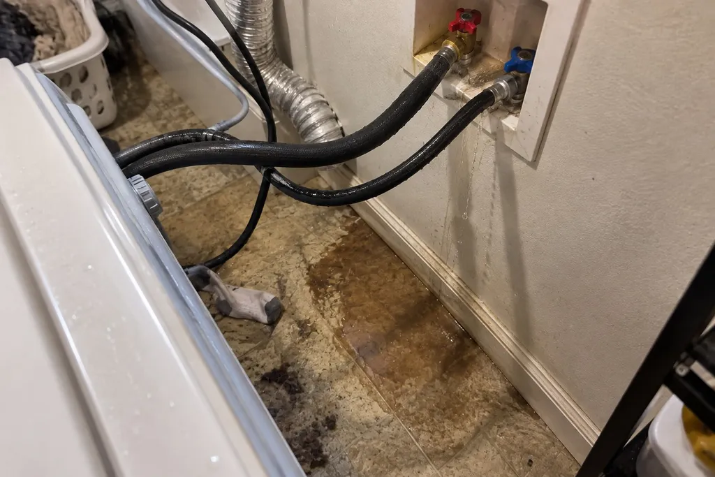 Washing machine pulled out to reveal a dripping fill hose and stained floor