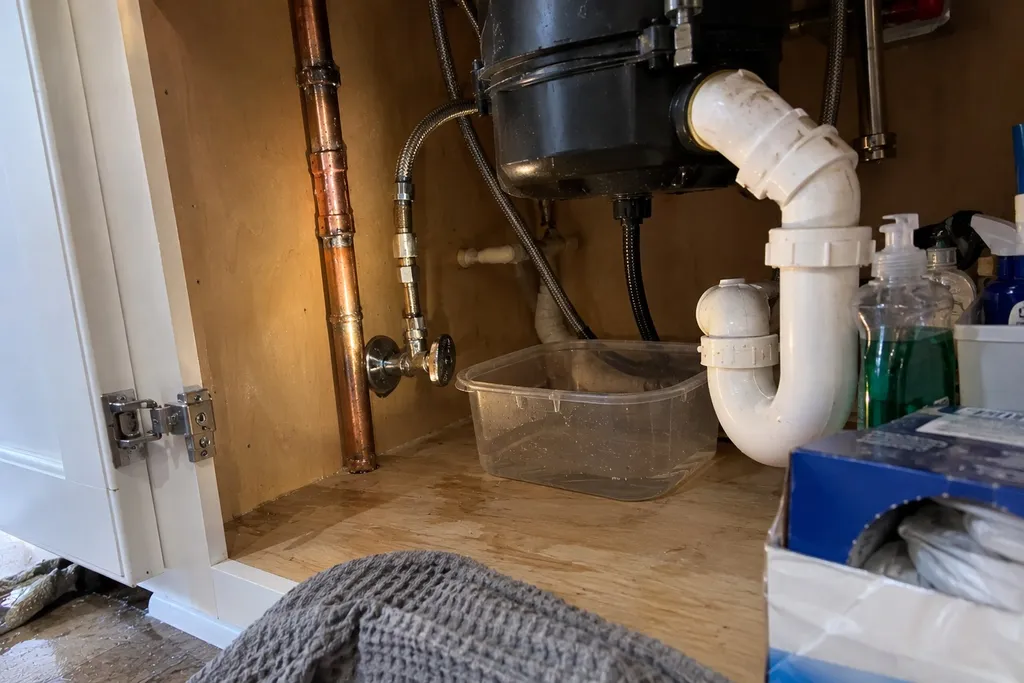 New soldered copper fitting under a Troutdale kitchen sink, a small tub catching a minor trap drip